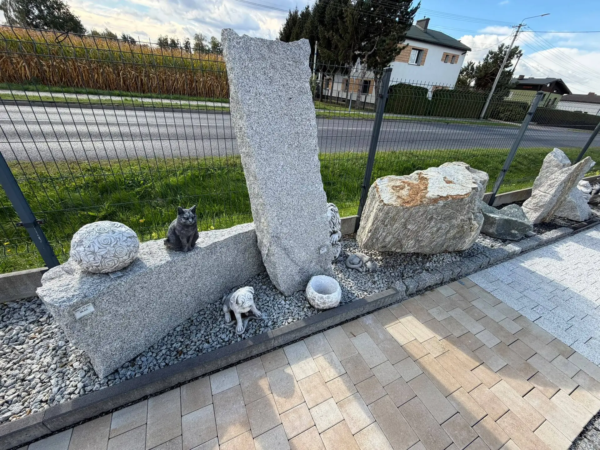 Głazy granitowe i figurki na rabacie przy ogrodzeniu